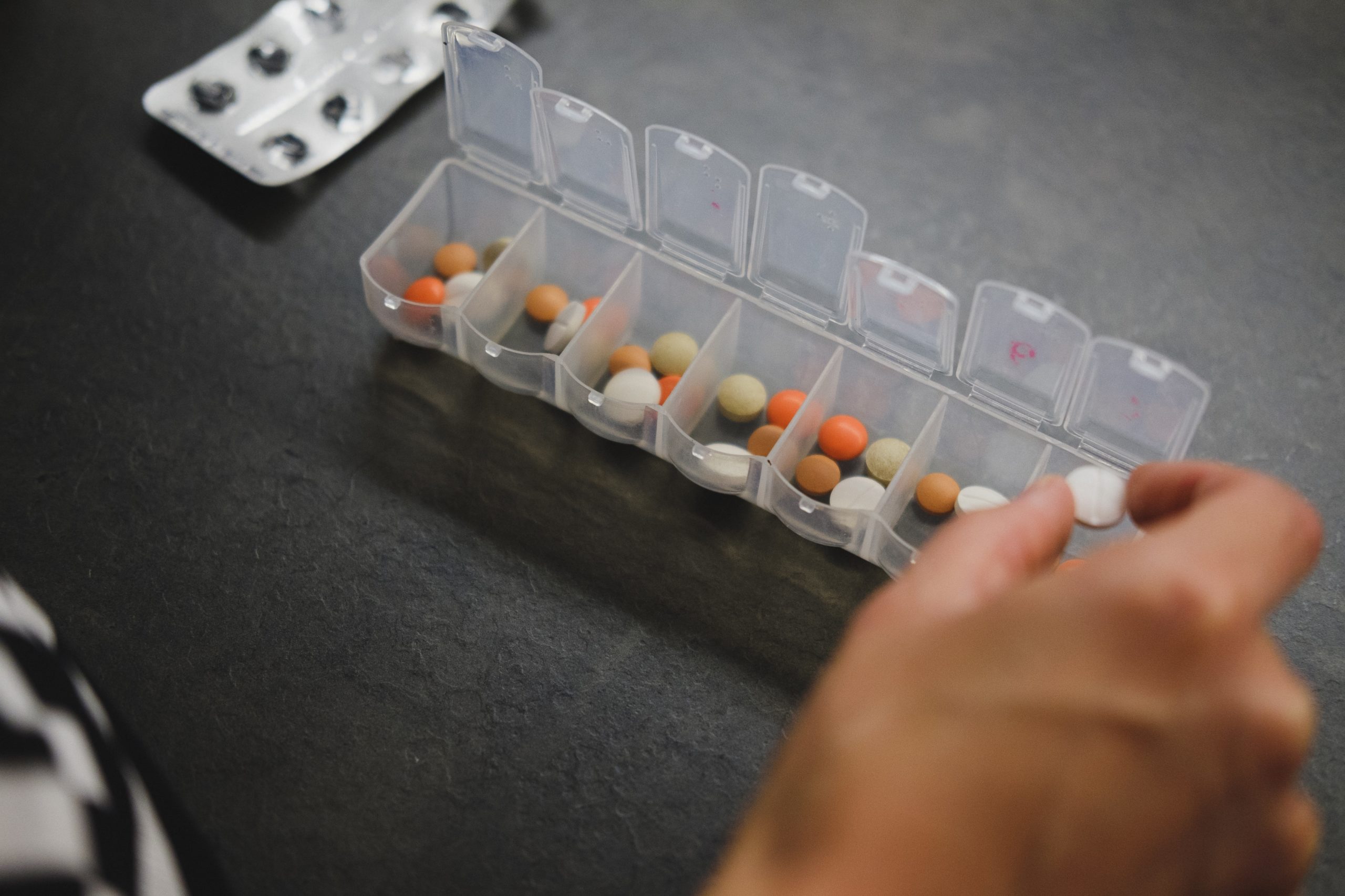 A person taking pills out of an open pill organizer.