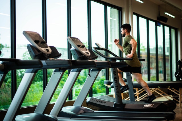 A man runs a treadmill in a gym while looking outside